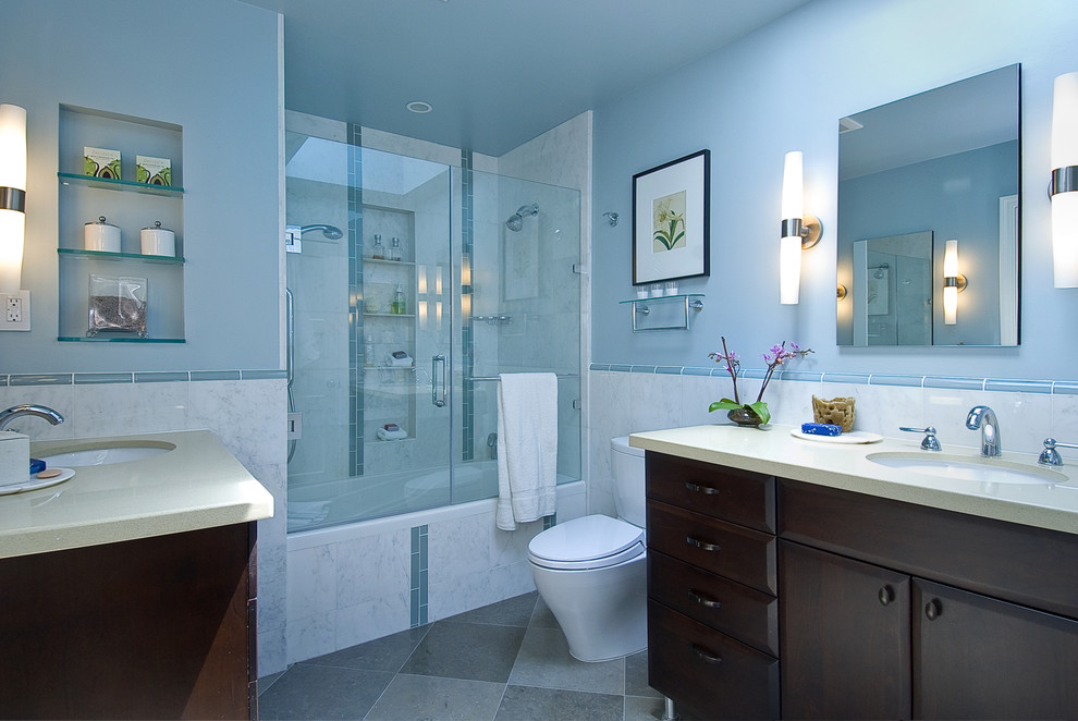 This is an example of a mid-sized traditional master bathroom in Auckland with furniture-like cabinets, brown cabinets, a drop-in tub, a shower/bathtub combo, a one-piece toilet, gray tile, stone tile, blue walls, limestone floors, an undermount sink and engineered quartz benchtops.