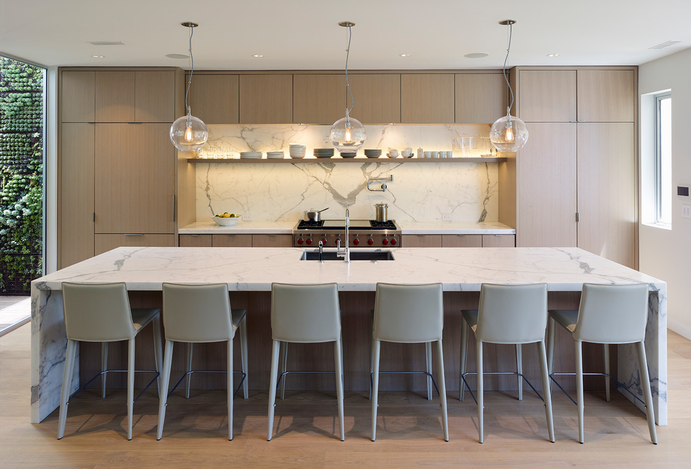 Photo of a contemporary kitchen in San Francisco with an undermount sink, flat-panel cabinets, light wood cabinets, white splashback, stone slab splashback, stainless steel appliances, light hardwood floors, with island, beige floor and white benchtop.