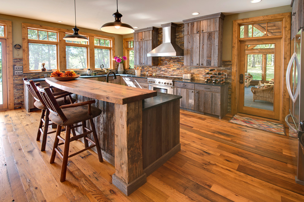 Large mountain style l-shaped medium tone wood floor and brown floor eat-in kitchen photo with an island, an undermount sink, flat-panel cabinets, dark wood cabinets, soapstone countertops, multicolored backsplash, stone tile backsplash and stainless steel appliances