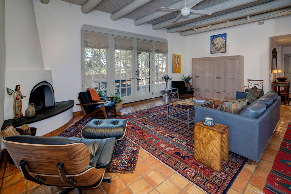 Mid-sized eclectic open concept living room in Albuquerque with white walls, terra-cotta floors, a corner fireplace, a plaster fireplace surround, a concealed tv and orange floor.