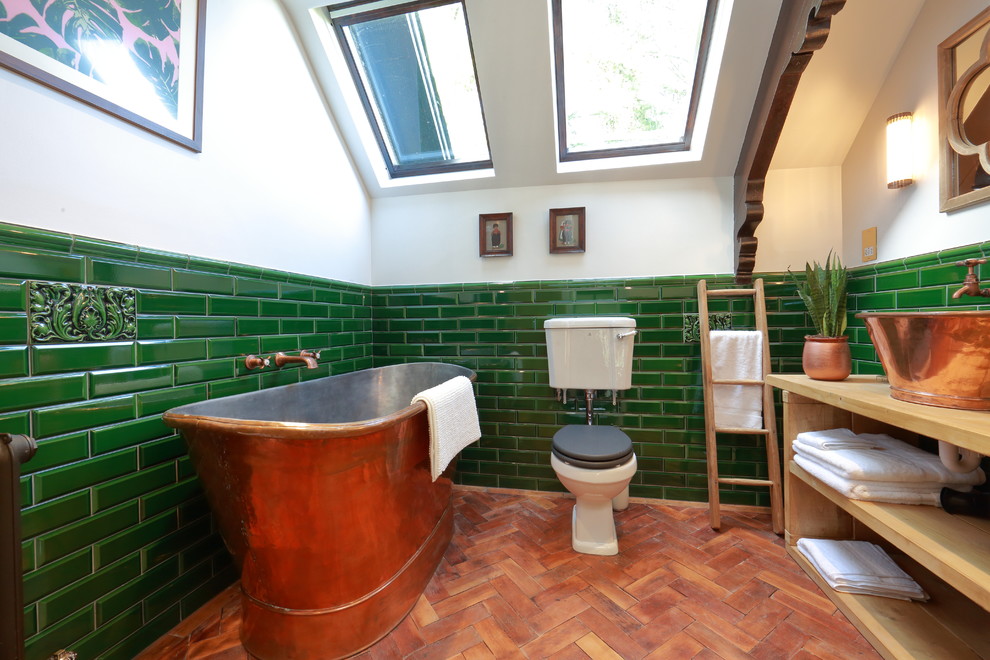 Mid-sized traditional master bathroom in London with open cabinets, light wood cabinets, a freestanding tub, a two-piece toilet, green tile, subway tile, white walls, a vessel sink, wood benchtops, orange floor and medium hardwood floors.