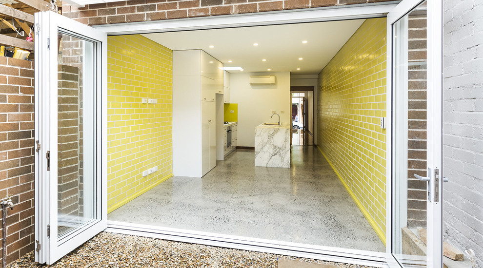 Small contemporary galley eat-in kitchen in Sydney with marble benchtops, yellow splashback, glass sheet splashback, white appliances, a double-bowl sink, concrete floors and with island.