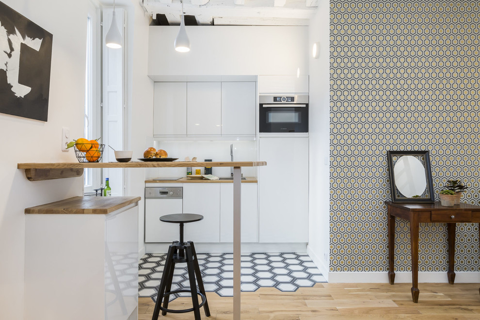 Inspiration for a scandinavian single-wall open plan kitchen in Paris with flat-panel cabinets, white cabinets, wood benchtops, stainless steel appliances, multi-coloured floor, brown benchtop, an undermount sink, white splashback, glass tile splashback, cement tiles and no island.