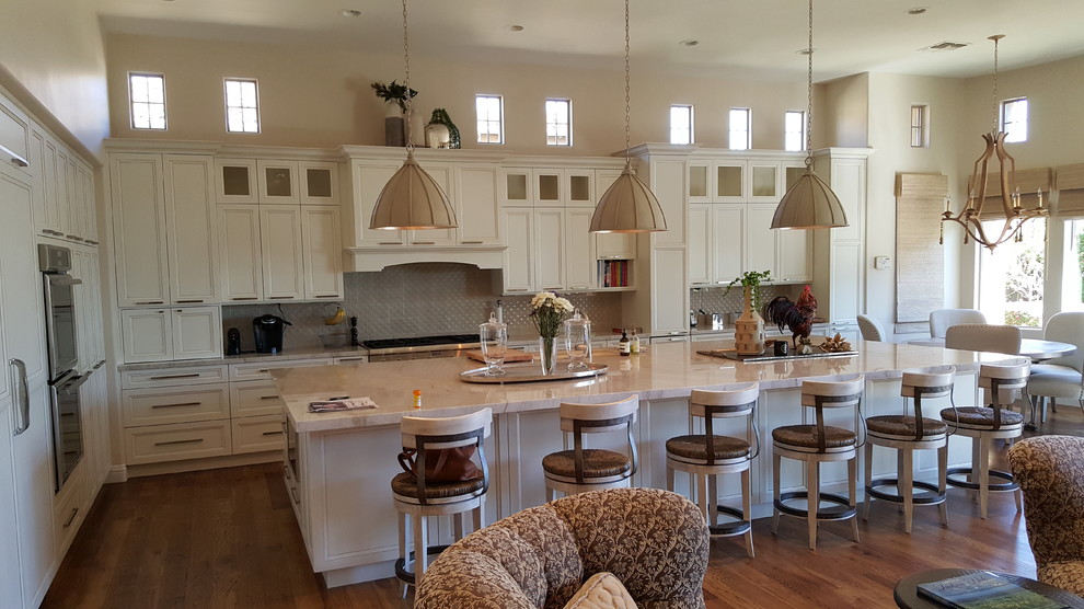 Large transitional l-shaped dark wood floor and brown floor eat-in kitchen photo in Orange County with recessed-panel cabinets, white cabinets, granite countertops, paneled appliances, an island and gray backsplash