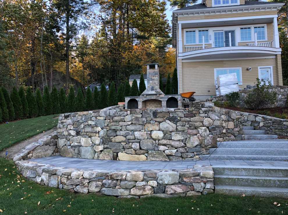 Large eclectic sloped full sun formal garden in Boston with with fireplace and concrete pavers for summer.