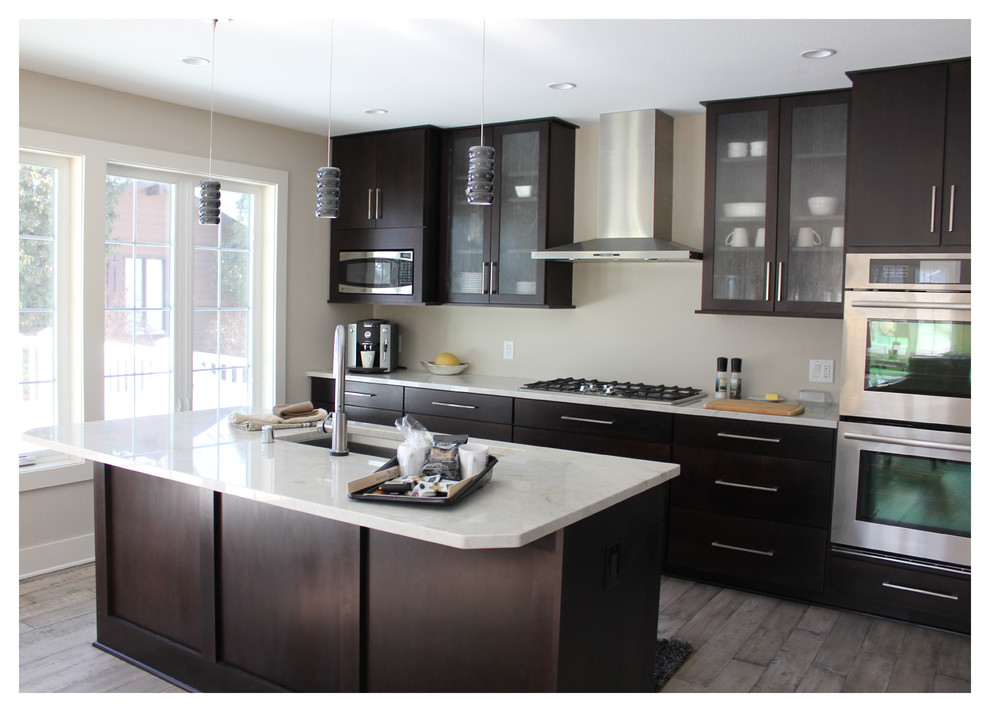 This is an example of a mid-sized modern l-shaped eat-in kitchen in Milwaukee with an undermount sink, glass-front cabinets, dark wood cabinets, limestone benchtops, beige splashback, stainless steel appliances, dark hardwood floors and with island.