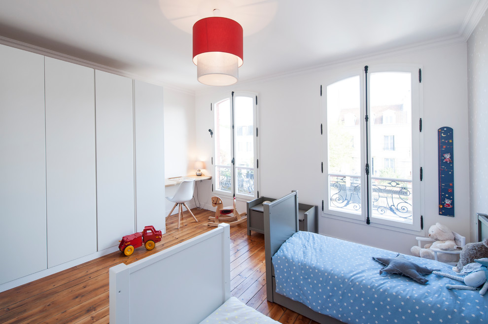 Photo of a scandinavian gender-neutral kids' bedroom for kids 4-10 years old in Paris with white walls, medium hardwood floors and brown floor.