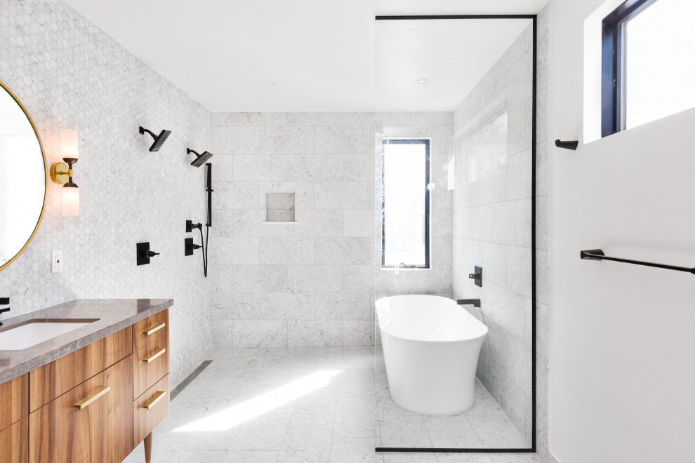 This is an example of a large contemporary ensuite bathroom in Denver with flat-panel cabinets, medium wood cabinets, a freestanding bath, a built-in shower, a one-piece toilet, white tiles, marble tiles, white walls, marble flooring, a submerged sink, limestone worktops, white floors, an open shower, grey worktops, an enclosed toilet, double sinks and a floating vanity unit.