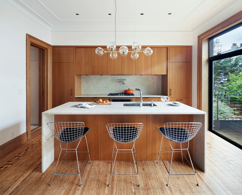 This is an example of a contemporary galley kitchen in New York with an undermount sink, flat-panel cabinets, medium wood cabinets, white splashback, medium hardwood floors, with island and panelled appliances.