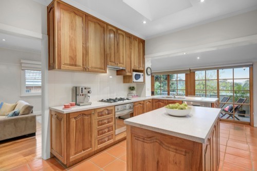 This is an example of a mid-sized contemporary l-shaped separate kitchen in Melbourne with a double-bowl sink, raised-panel cabinets, medium wood cabinets, quartz benchtops, white splashback, ceramic splashback, stainless steel appliances, terra-cotta floors, with island, orange floor and white benchtop.