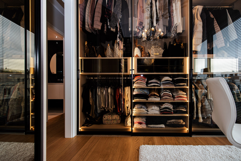 This is an example of a mid-sized contemporary dressing room with glass-front cabinets, light hardwood floors and brown floor.