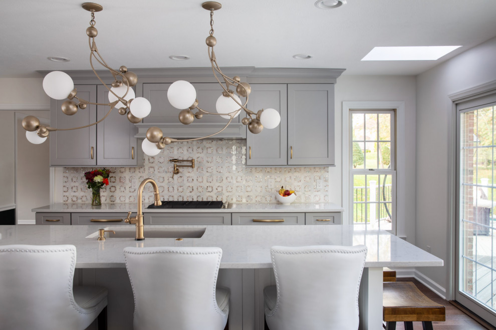 Inspiration for a transitional dark wood floor and brown floor kitchen remodel with a drop-in sink, shaker cabinets, gray cabinets, quartzite countertops, white backsplash, mosaic tile backsplash, stainless steel appliances, an island and white countertops