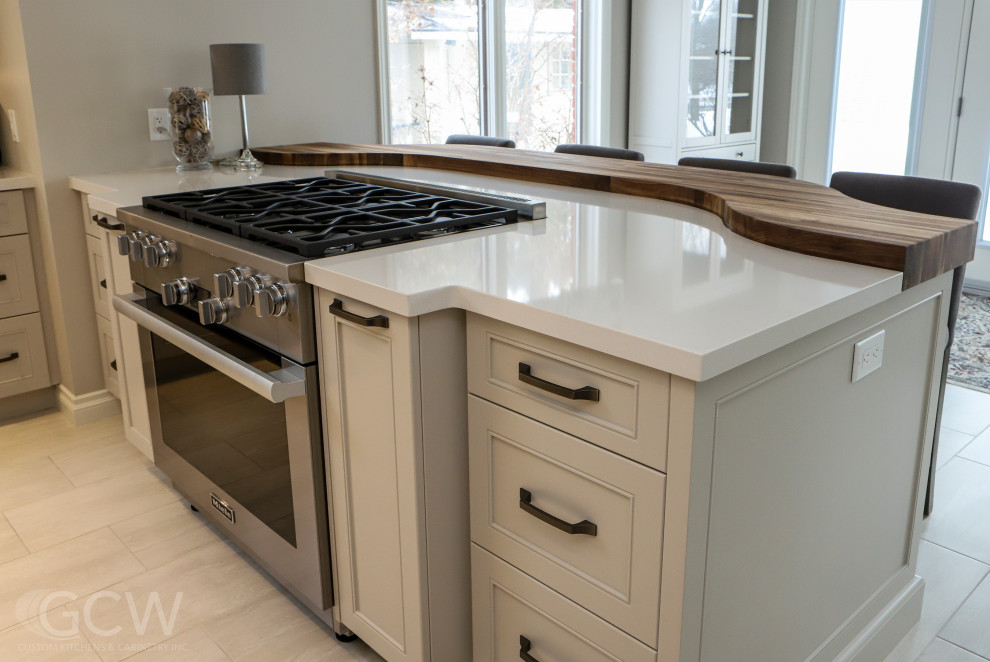 This is an example of a large contemporary l-shaped eat-in kitchen in Toronto with an undermount sink, shaker cabinets, beige cabinets, quartz benchtops, white splashback, ceramic splashback, stainless steel appliances, ceramic floors, with island, beige floor and beige benchtop.