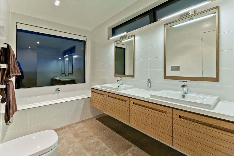Design ideas for a large contemporary bathroom in Auckland with beaded inset cabinets, medium wood cabinets, an undermount tub, a wall-mount toilet, white tile, ceramic tile, white walls, terra-cotta floors, a trough sink and granite benchtops.