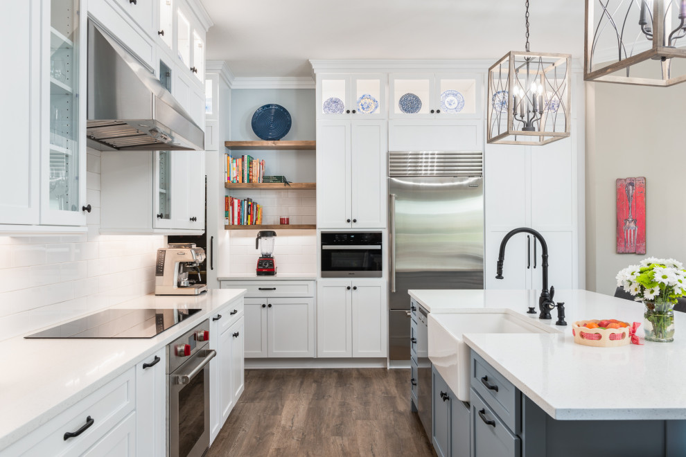 Design ideas for a large classic l-shaped open plan kitchen in Tampa with a belfast sink, shaker cabinets, white cabinets, engineered stone countertops, white splashback, metro tiled splashback, stainless steel appliances, vinyl flooring, an island, brown floors and white worktops.