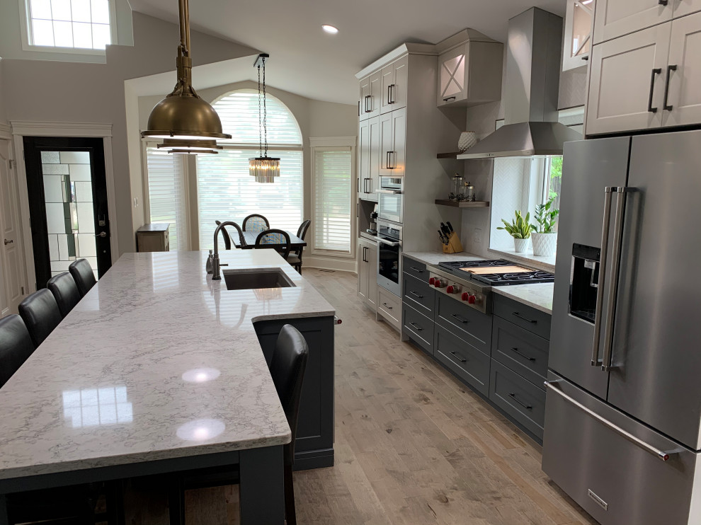 Inspiration for a large transitional galley light wood floor, brown floor and vaulted ceiling eat-in kitchen remodel with an undermount sink, shaker cabinets, white cabinets, quartzite countertops, white backsplash, ceramic backsplash, stainless steel appliances, an island and white countertops