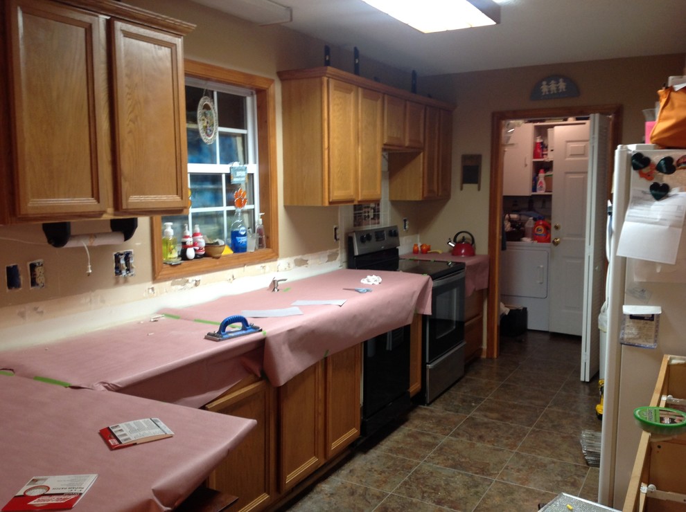 Example of a l-shaped eat-in kitchen design with an undermount sink, flat-panel cabinets, brown backsplash, glass tile backsplash, stainless steel appliances and a peninsula