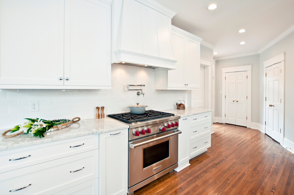 Design ideas for a mid-sized transitional galley eat-in kitchen in Nashville with a farmhouse sink, shaker cabinets, white cabinets, marble benchtops, white splashback, cement tile splashback, stainless steel appliances, medium hardwood floors and no island.