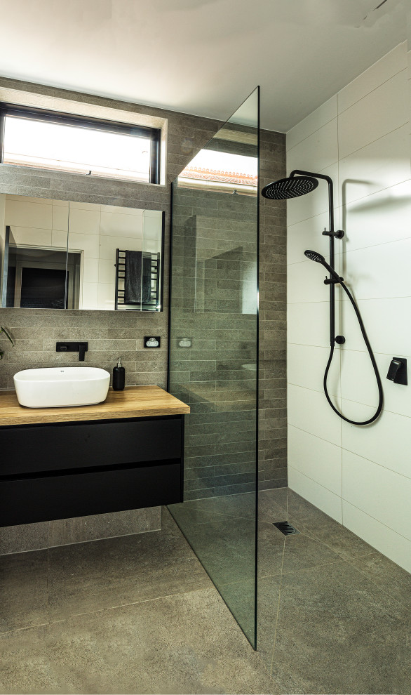 Photo of a mid-sized modern kids bathroom in Melbourne with glass-front cabinets, black cabinets, an open shower, a one-piece toilet, gray tile, ceramic tile, white walls, cement tiles, a console sink, wood benchtops, grey floor and an open shower.