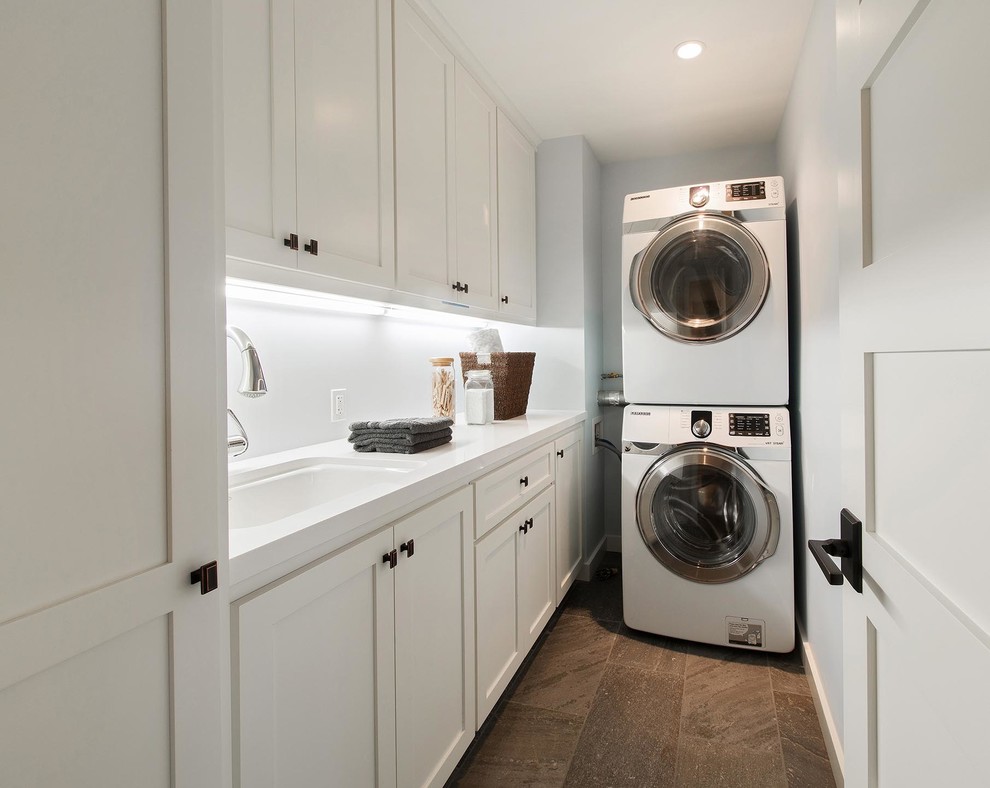 Photo of a small transitional l-shaped dedicated laundry room in San Francisco with an undermount sink, recessed-panel cabinets, white cabinets, quartz benchtops, blue walls, porcelain floors and a stacked washer and dryer.