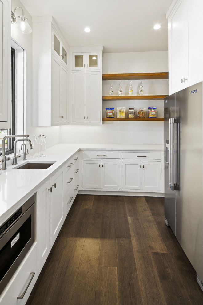 Design ideas for an expansive modern single-wall kitchen pantry in Portland with a drop-in sink, flat-panel cabinets, white cabinets, granite benchtops, white splashback, ceramic splashback, stainless steel appliances, medium hardwood floors, multiple islands, brown floor and white benchtop.