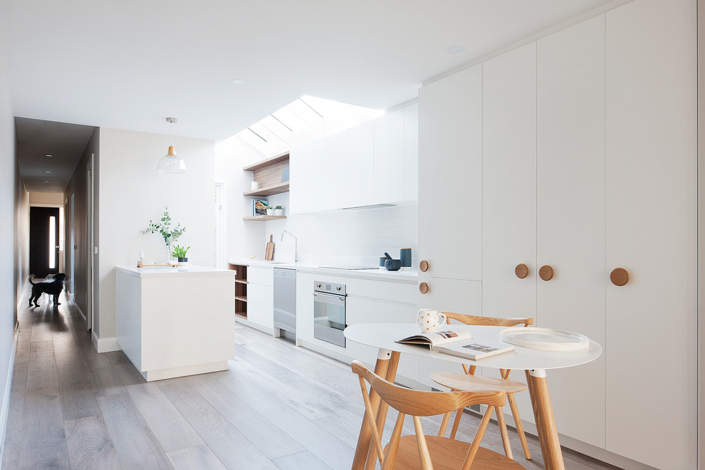 Photo of a large contemporary galley eat-in kitchen in Melbourne with a drop-in sink, beaded inset cabinets, white cabinets, white splashback, subway tile splashback, stainless steel appliances and with island.