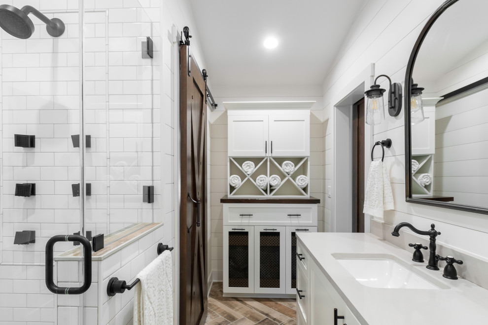 Пример оригинального дизайна: главная ванная комната среднего размера в стиле кантри с фасадами в стиле шейкер, белыми фасадами, душем в нише, белой плиткой, плиткой кабанчик, белыми стенами, деревянным полом, врезной раковиной, столешницей из искусственного кварца, коричневым полом, душем с распашными дверями, серой столешницей, нишей, тумбой под две раковины, встроенной тумбой и стенами из вагонки