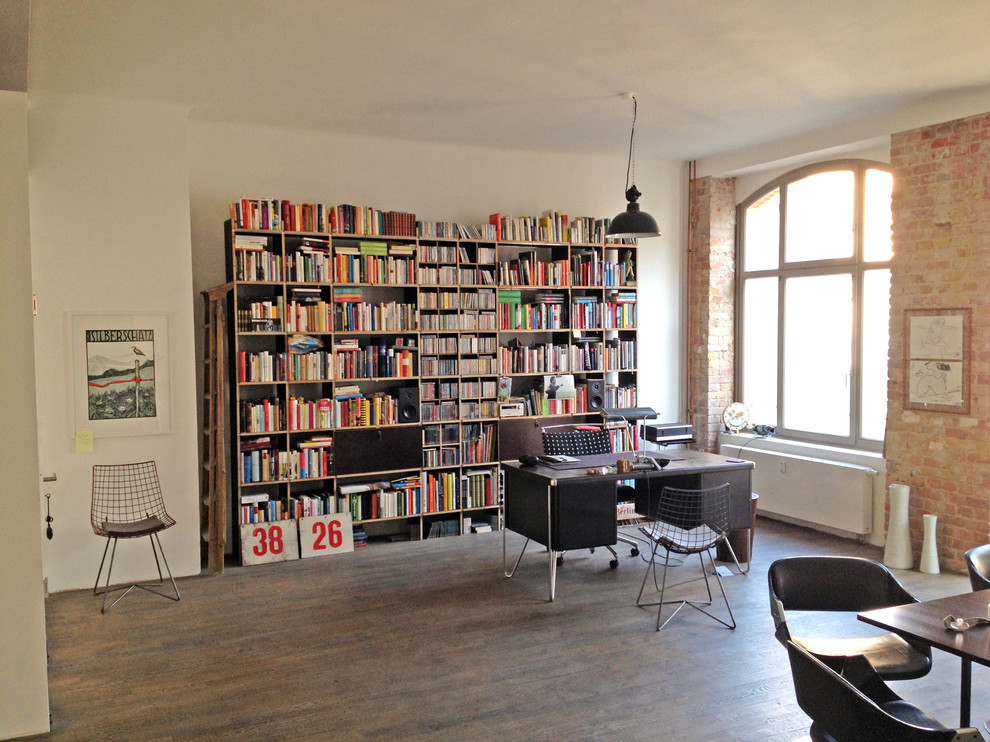 This is an example of a contemporary home office in Dortmund with a library, white walls, dark hardwood floors, a freestanding desk and brown floor.