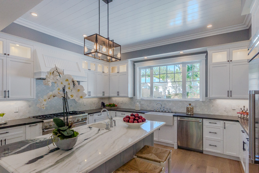 Design ideas for a large transitional u-shaped kitchen in Los Angeles with a farmhouse sink, recessed-panel cabinets, white cabinets, white splashback, stainless steel appliances, light hardwood floors and with island.