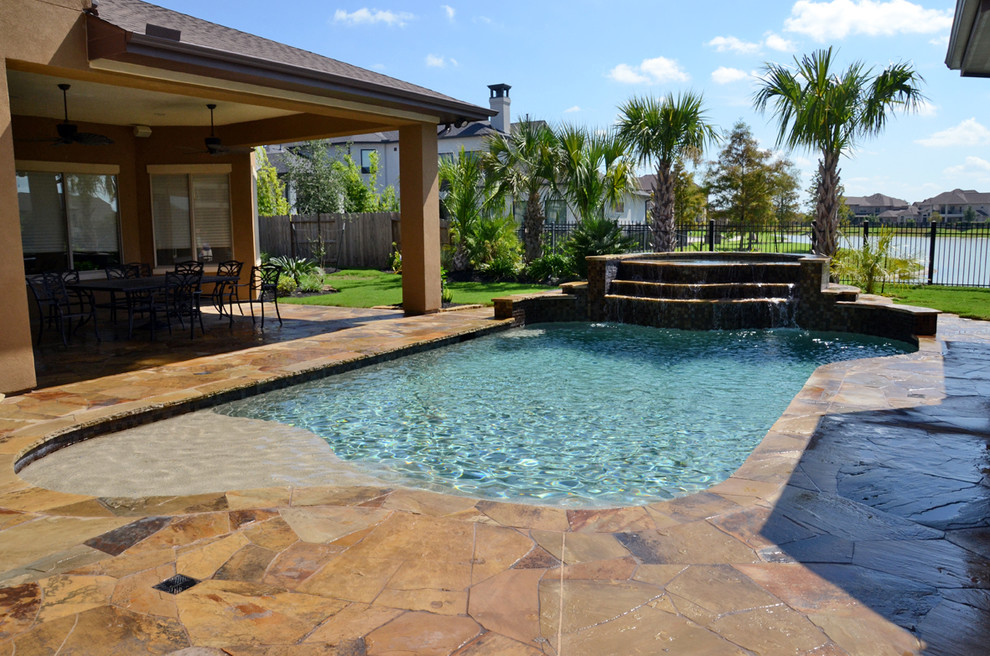 This is an example of a mid-sized mediterranean backyard custom-shaped pool in Houston with a hot tub and natural stone pavers.