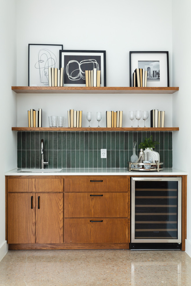 Photo of a midcentury single-wall wet bar in Dallas with an undermount sink, flat-panel cabinets, medium wood cabinets, quartzite benchtops, green splashback, glass tile splashback, concrete floors, grey floor and white benchtop.