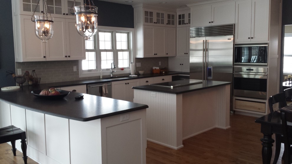 Large transitional u-shaped medium tone wood floor eat-in kitchen photo with an undermount sink, shaker cabinets, white cabinets, granite countertops, gray backsplash, ceramic backsplash, stainless steel appliances and gray walls