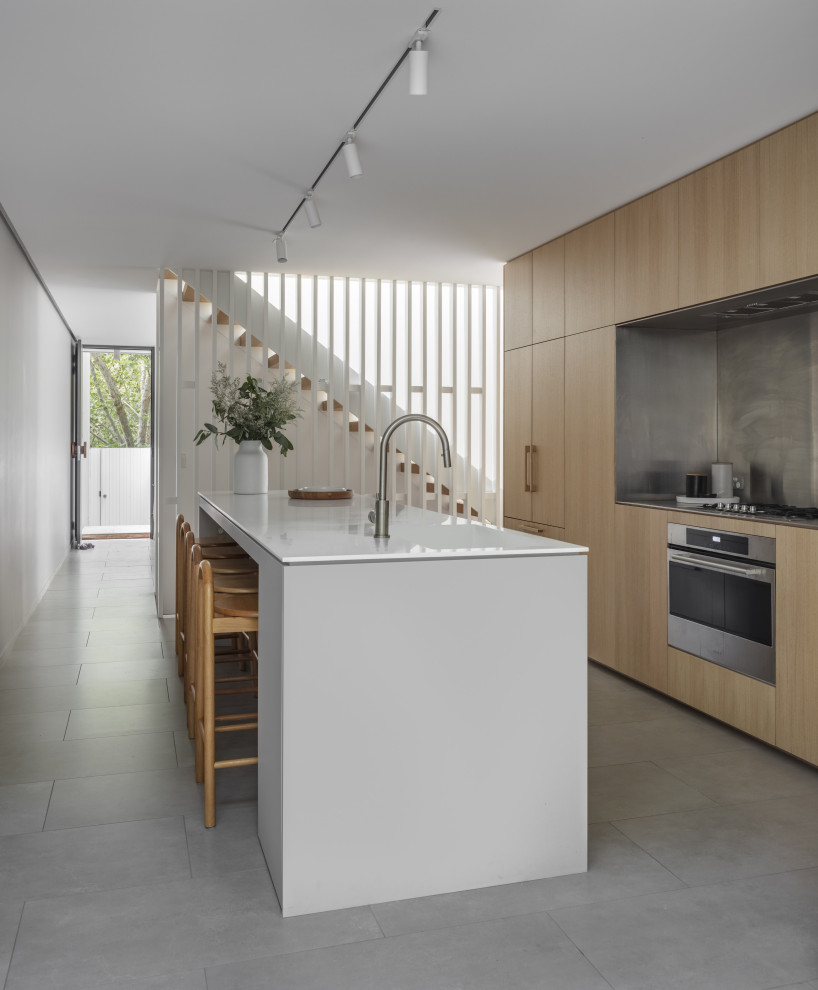 Foto de cocina moderna con armarios con paneles lisos, puertas de armario de madera clara, una isla, suelo gris y encimeras blancas