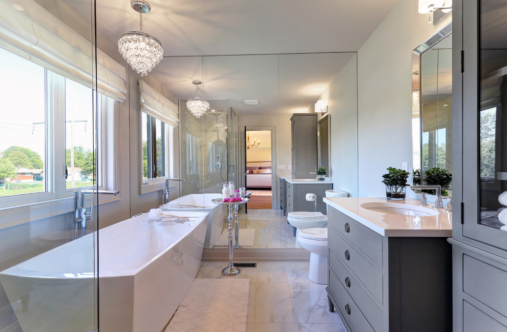 Mid-sized transitional master bathroom in Toronto with furniture-like cabinets, grey cabinets, a freestanding tub, an open shower, a two-piece toilet, white tile, porcelain tile, grey walls, porcelain floors, an undermount sink and engineered quartz benchtops.