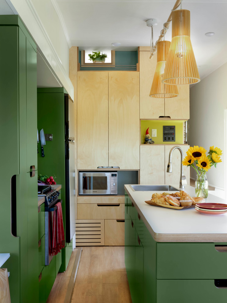 Inspiration for a small eclectic galley eat-in kitchen in Burlington with flat-panel cabinets, green cabinets, laminate benchtops, black splashback, stainless steel appliances, light hardwood floors, with island and a single-bowl sink.