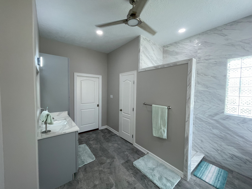 Cette image montre une salle de bain design avec un placard à porte shaker, des portes de placard grises, une baignoire indépendante, une douche ouverte, des carreaux de porcelaine, un sol en carrelage de porcelaine, un lavabo encastré, un plan de toilette en quartz modifié, un plan de toilette blanc, meuble double vasque et meuble-lavabo encastré.