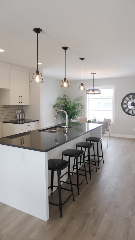 Inspiration for a small contemporary galley light wood floor eat-in kitchen remodel with an undermount sink, flat-panel cabinets, white cabinets, granite countertops, gray backsplash, ceramic backsplash and an island