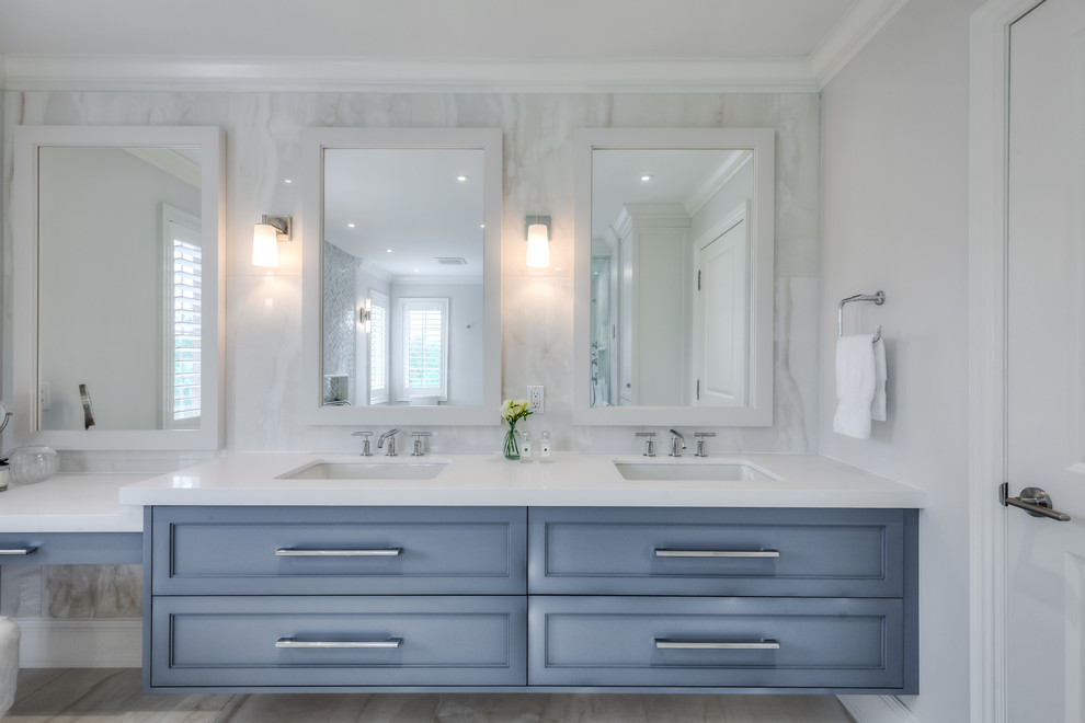 This is an example of a mid-sized transitional master bathroom in Toronto with shaker cabinets, blue cabinets, a freestanding tub, a curbless shower, a one-piece toilet, beige tile, porcelain tile, white walls, porcelain floors, an undermount sink, quartzite benchtops, beige floor and a hinged shower door.