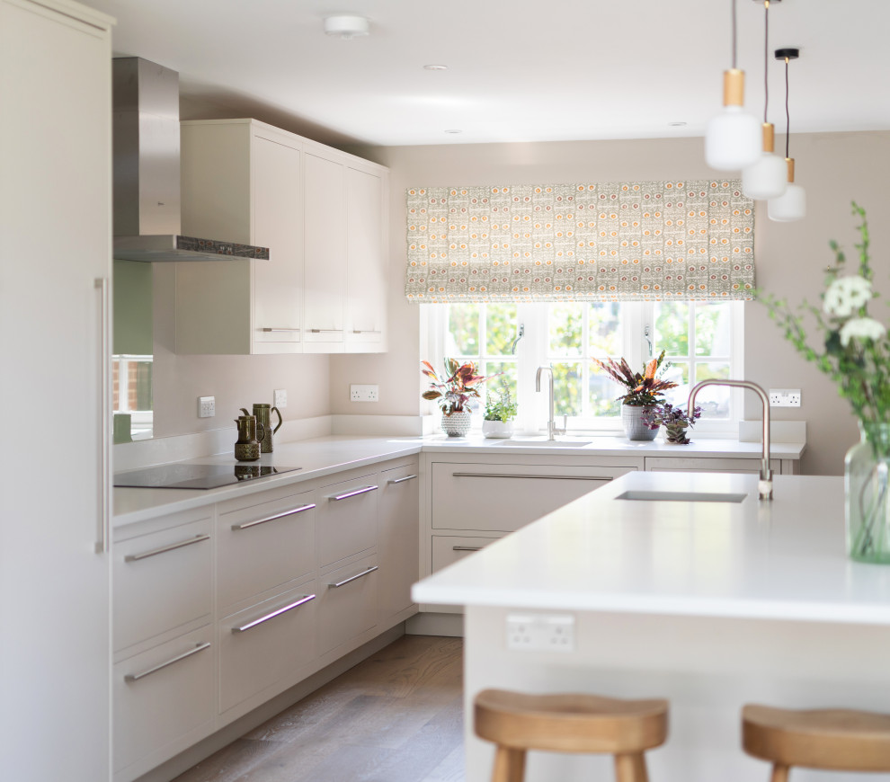 Bild på ett mellanstort funkis vit vitt kök, med en dubbel diskho, släta luckor, grå skåp, bänkskiva i kvartsit, grönt stänkskydd, glaspanel som stänkskydd, rostfria vitvaror, ljust trägolv, en köksö och brunt golv