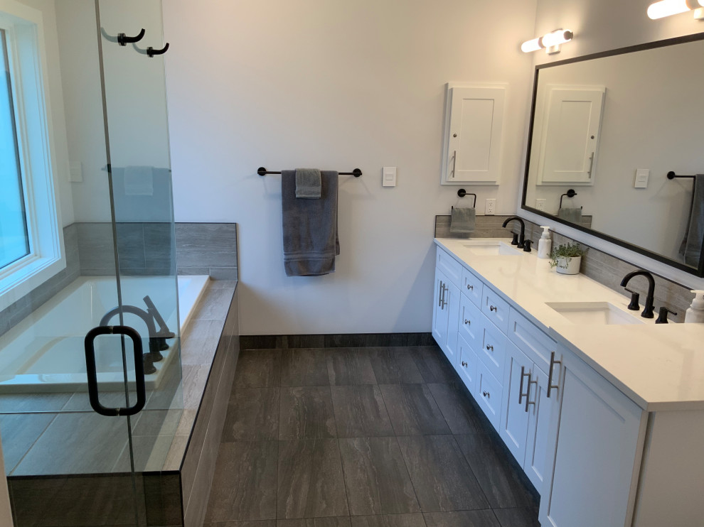 Photo of a large contemporary master bathroom in Other with shaker cabinets, white cabinets, a drop-in tub, a corner shower, a one-piece toilet, gray tile, porcelain tile, white walls, porcelain floors, an undermount sink, engineered quartz benchtops, grey floor, a hinged shower door and white benchtops.