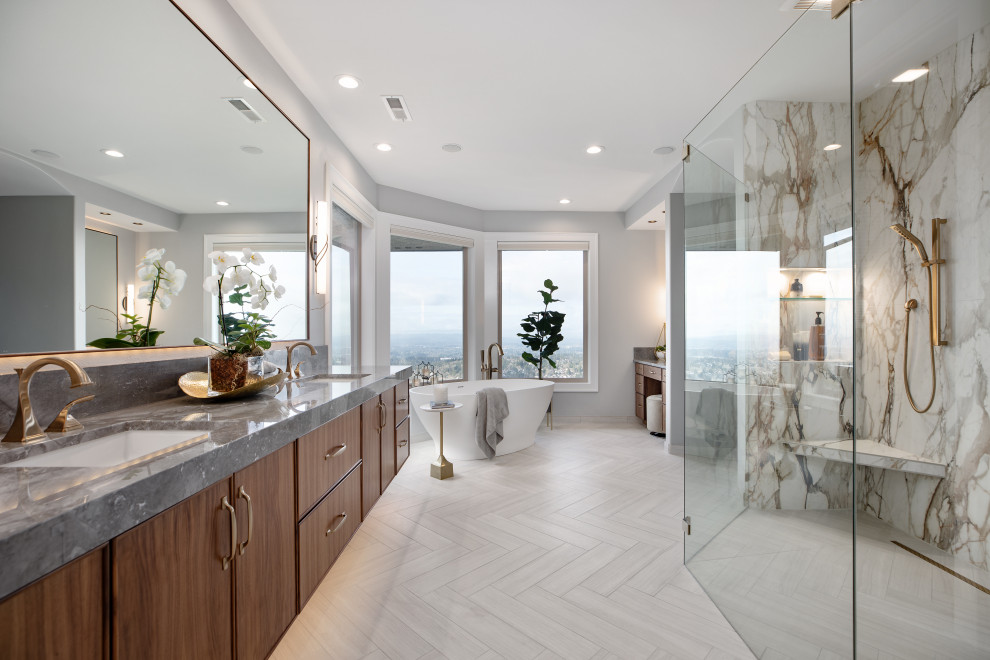 Photo of a large contemporary master bathroom in Portland with medium wood cabinets, a freestanding tub, a curbless shower, porcelain floors, an undermount sink, marble benchtops, beige floor, an open shower, grey benchtops, an enclosed toilet, a double vanity, a floating vanity, grey walls and flat-panel cabinets.