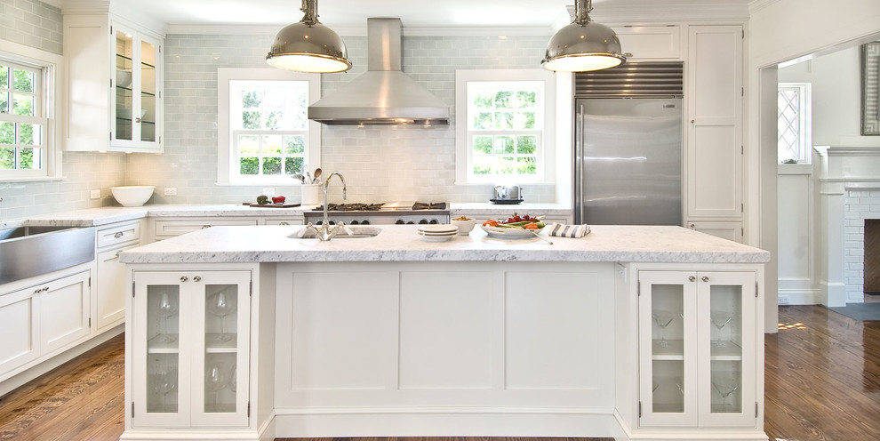 Inspiration for a large traditional l-shaped eat-in kitchen in New York with a farmhouse sink, glass-front cabinets, white cabinets, granite benchtops, grey splashback, glass tile splashback, stainless steel appliances, dark hardwood floors and with island.