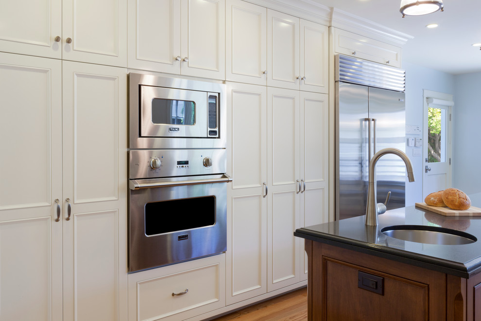 Photo of a large traditional galley separate kitchen in Phoenix with an undermount sink, recessed-panel cabinets, white cabinets, quartz benchtops, blue splashback, stainless steel appliances, medium hardwood floors, with island and subway tile splashback.