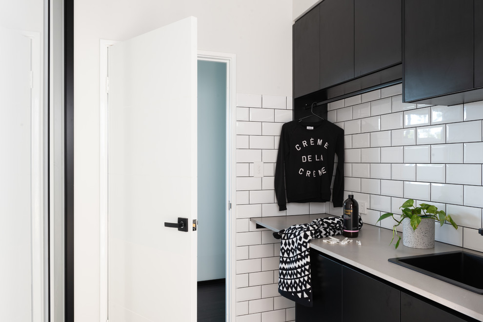 This is an example of an industrial dedicated laundry room in Perth with a drop-in sink, black cabinets, quartz benchtops, ceramic floors, a stacked washer and dryer, grey floor and grey benchtop.