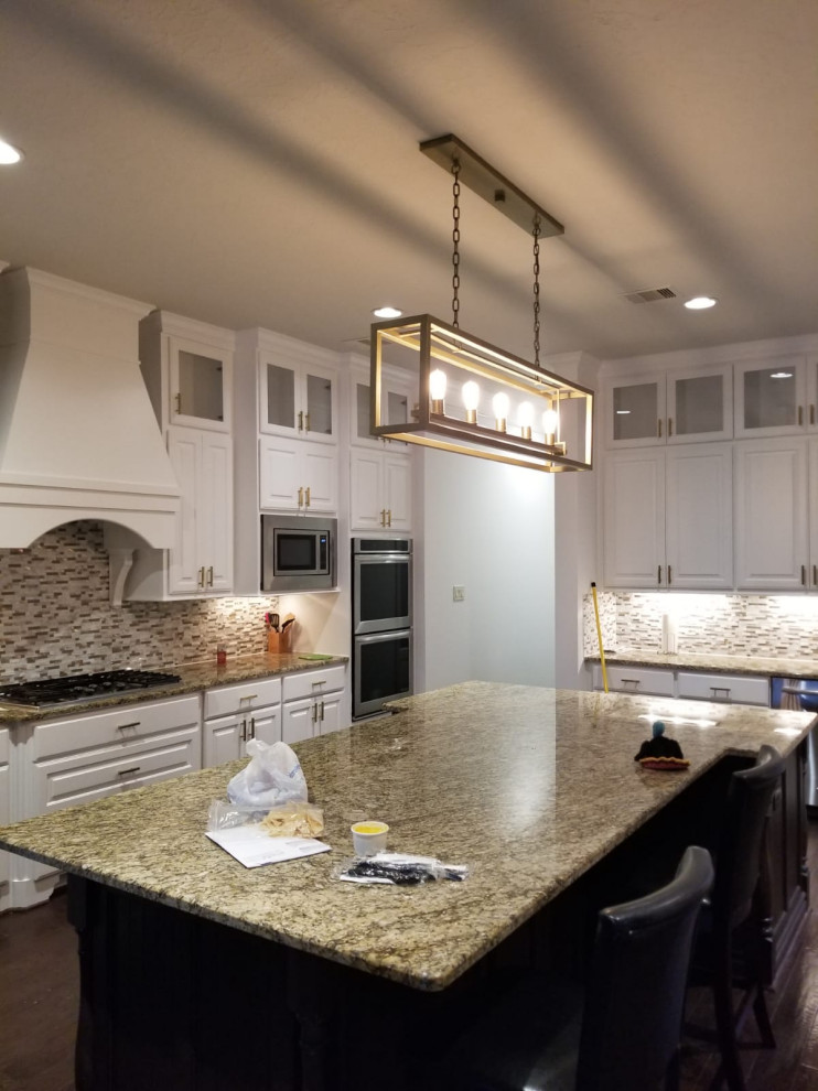 Large u-shaped open plan kitchen in Houston with a double-bowl sink, shaker cabinets, white cabinets, marble benchtops, multi-coloured splashback, marble splashback, stainless steel appliances, laminate floors, with island, brown floor, white benchtop and coffered.