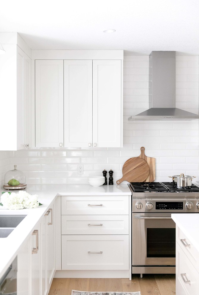 Large transitional u-shaped medium tone wood floor and brown floor eat-in kitchen photo in Calgary with an undermount sink, shaker cabinets, white cabinets, quartzite countertops, white backsplash, subway tile backsplash, stainless steel appliances, an island and white countertops