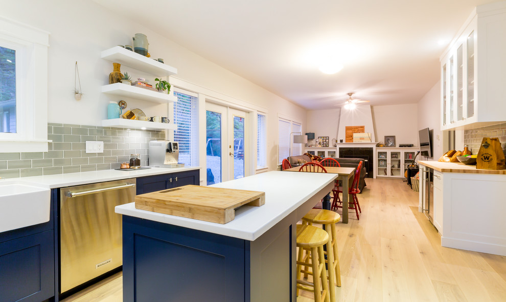 Open concept kitchen - large transitional u-shaped light wood floor open concept kitchen idea with a farmhouse sink, shaker cabinets, blue cabinets, quartz countertops, gray backsplash, glass tile backsplash, stainless steel appliances and an island
