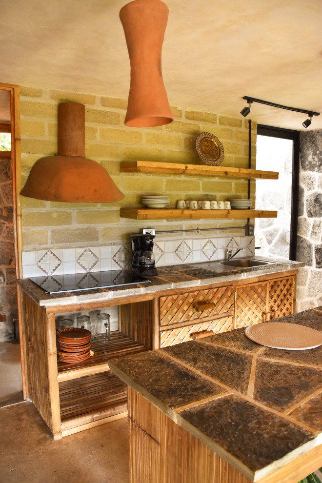 Photo of a medium sized rustic galley enclosed kitchen in Other with a single-bowl sink, open cabinets, light wood cabinets, wood worktops, grey splashback, mosaic tiled splashback, black appliances, concrete flooring, an island, brown floors and grey worktops.