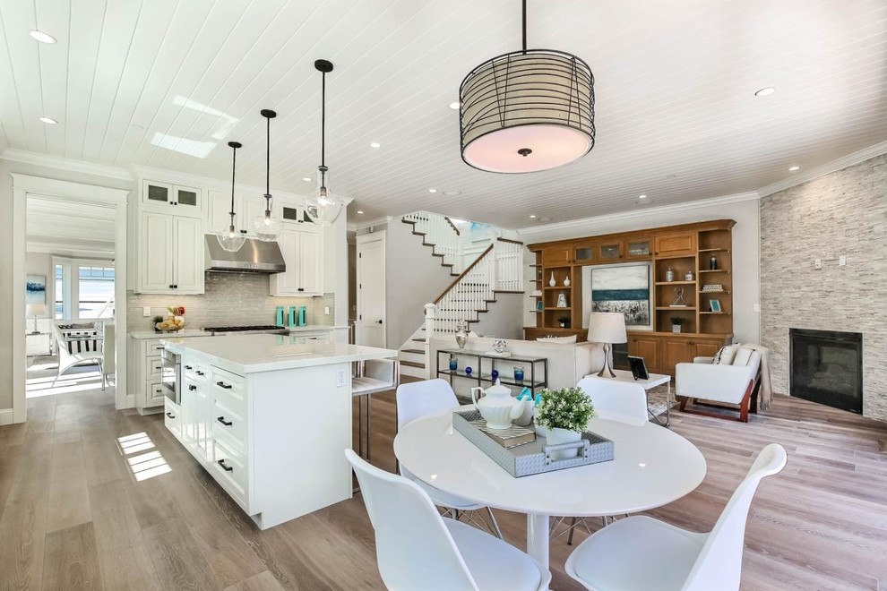 Photo of a mid-sized arts and crafts l-shaped open plan kitchen in San Francisco with a farmhouse sink, raised-panel cabinets, white cabinets, quartz benchtops, grey splashback, glass tile splashback, stainless steel appliances, medium hardwood floors, with island and grey floor.
