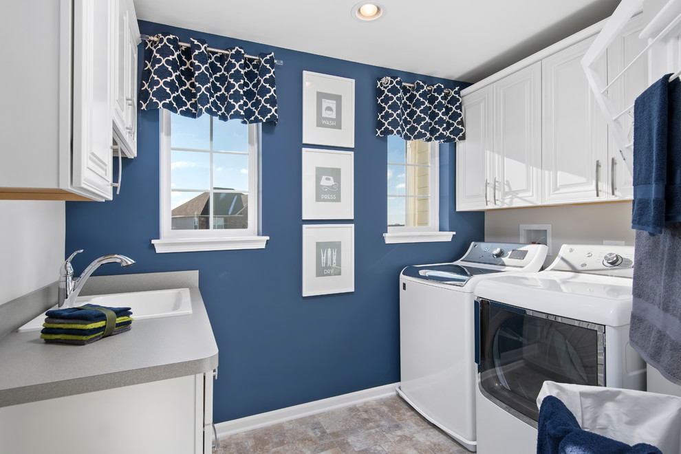 Photo of a mid-sized transitional galley dedicated laundry room in Chicago with a drop-in sink, raised-panel cabinets, white cabinets, laminate benchtops, blue walls, porcelain floors and a side-by-side washer and dryer.